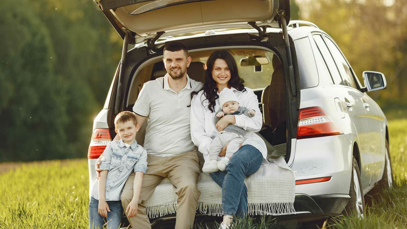 Glückliche Familie genießt ein Picknick im Grünen neben ihrem geräumigen Familienauto